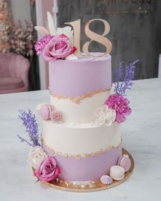 a three tiered cake with flowers and feathers on the top is decorated in gold