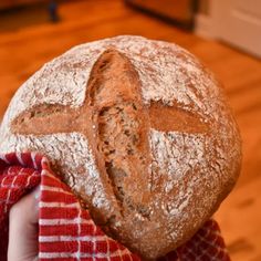 a person holding a loaf of bread in front of their face with a cross on it