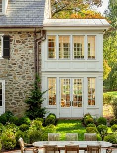 an outdoor dining table and chairs in front of a stone house with white trim on the windows