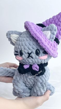 a hand holding a small gray and purple crocheted cat with a hat on it's head