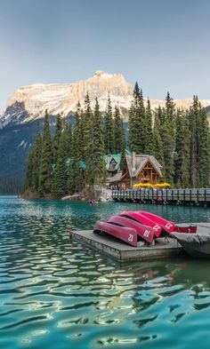 two canoes are tied up on the dock in front of a mountain lake with pine trees