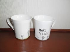 two coffee mugs sitting on top of a wooden table next to each other with writing on them