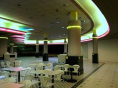 tables and chairs are lined up in an empty room with colorful lights on the ceiling