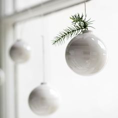 three white ornaments hanging from the ceiling in front of a window with pine needles on them