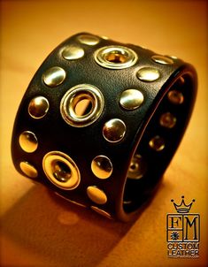 a black leather bracelet with gold studs on the outside and inside, sitting on a table