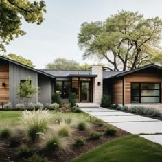 a modern house with wood siding and stone walkway leading to the front door, grass lawning and trees