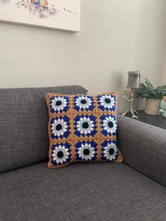 a blue and white crocheted pillow sitting on top of a gray couch next to a potted plant