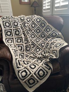 a crocheted afghan sits on a leather chair in front of a window with shutters