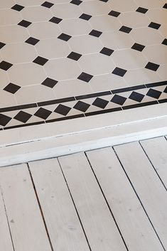 a white toilet sitting next to a black and white tile floor in a bathroom with wooden floors