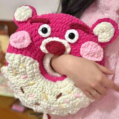 a woman holding a crocheted pink and white donut shaped animal head purse