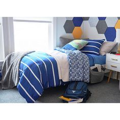 a bedroom with blue and white bedding, striped comforter on the floor and yellow hexagonal wallpaper