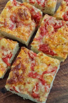 several square pieces of pizza sitting on top of a wooden cutting board