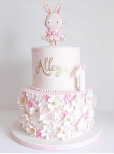 a pink and white cake with an animal on top that says allegine surrounded by flowers