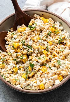 a bowl filled with corn and cheese on top of a table next to a wooden spoon