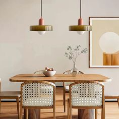 a dining room table with chairs and a bowl of fruit on it in front of two hanging lights