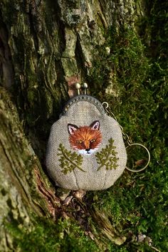 a coin purse with a fox on it hanging from a mossy tree trunk in the woods