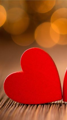 two red hearts sitting next to each other on top of a wooden table with lights in the background