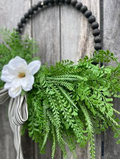 a wreath with flowers and greenery hanging on a wooden wall next to a black beaded necklace