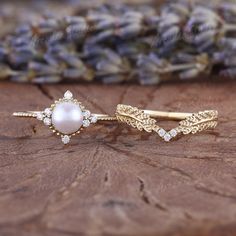 two gold rings with pearls and diamonds on top of a piece of wood next to lavender flowers