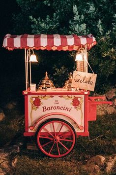 an old fashioned ice cream cart with lights on the top is sitting in front of some rocks