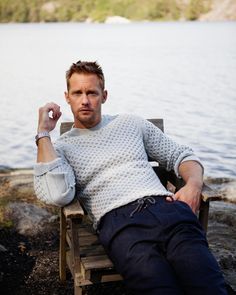 a man sitting on a wooden bench next to a lake and holding his arm up in the air