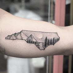 a tattoo with mountains and trees on the arm