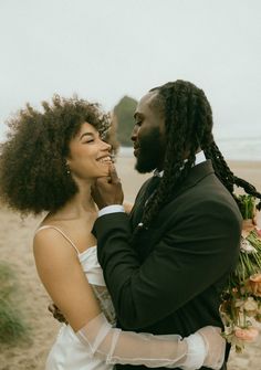 a man and woman standing next to each other on a beach with flowers in their hair