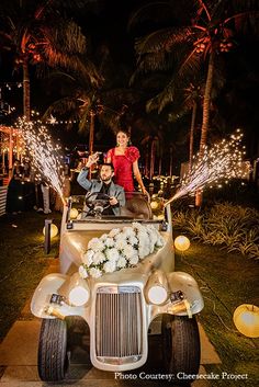 a man and woman are riding in an old car with lights on the side at night