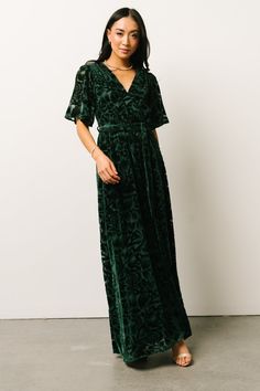 a woman wearing a green velvet dress and sandals standing in front of a white wall