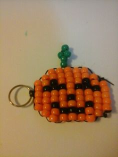 an orange and black beaded pumpkin keychain on a white surface with a green hook