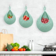 three bags hanging on the wall over a stove top with fruits and vegetables in them