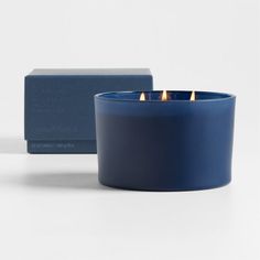 a blue candle sitting next to a box on a white surface with two candles in it