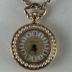 Vintage Bucherer 17 Jewel Swiss Pearl Pendant Watch Black Roman Numerals On White Background With Engrave Center Section Round Shape With Necklace And 24 Inch 925 Italian 2mm Necklace Gold Plated Or Vermeil Rope Necklace Vintage Pendant Watch Is Meticulously Enhanced With Pearl Bezel On Front. The Reverse Also Has A Pearl Bezel And There Is An Dark Blue Enamel Center With A Gold Leaf Floral Motif Design The Watch Has A Mineral Crystal Face Pearls May Be Flux Man Made Excellent Working Condition Elegant Evening Pocket Watch With Chronometer, Elegant White Pocket Watch For Formal Occasions, Elegant White Pocket Watch For Formal Events, Elegant Round Pocket Watch For Evening, Elegant Evening Pocket Watch, Elegant Gold Pocket Watch For Evening, Elegant Yellow Gold Pocket Watch, Face Pearls, Vintage Metal Pearl Necklace Gift