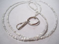 This simple single strand lightweight lanyard has a white and silver Mix of seed beads.   Lanyard is made with durable multi-strand coated beading wire and glass seed beads. Includes a 3/4" diameter key ring and a 7/8" long clip.  SELECT YOUR SIZE:  SMALL- Seed bead strand measures approximately 30". Approximately 17" from back of neck to bottom of clip.  MEDIUM- Seed bead strand measures approximately 33". Approximately 181/2" from back of neck to bottom of clip.  LARGE- Seed bead strand measures approximately 36". Approximately 20" from back of neck to bottom of clip.  *If no size is indicated at checkout we will ship size MEDIUM.*   Lanyards can be used to hold work or school ID badges, eyeglasses or sunglasses, keys, flash drives, life alert sensors, or whatever else you wish! They mak Seed Bead Lanyard, Bead Lanyard, Unique Beaded Jewelry, Lanyard Teacher, Beaded Lanyard, Teacher Lanyard, Crimp Beads, Beaded Lanyards, Beading Wire