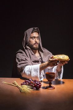 a man in a robe is holding a bread and some grapes on a wooden table