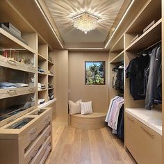 a walk in closet filled with lots of drawers and shelves next to a window that has a chandelier hanging from the ceiling