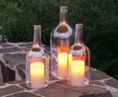 three bottles with lit candles in them sitting on a stone ledge next to some bushes