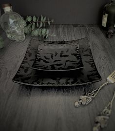 two black plates sitting on top of a wooden table next to silverware and bottles