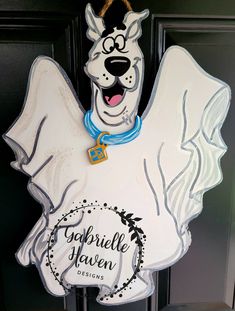 a white dog with a blue collar and name tag hanging on a door