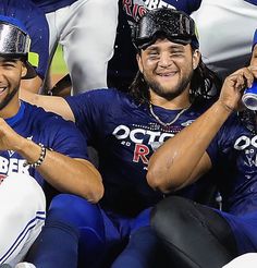 three baseball players are sitting on the bench and one is holding a water bottle in his hand