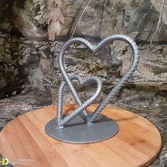 a metal heart sculpture sitting on top of a wooden table next to a stone wall