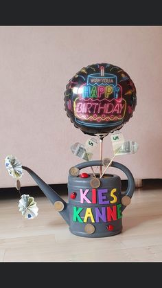 a watering can with a happy birthday balloon on top and money sticking out of it