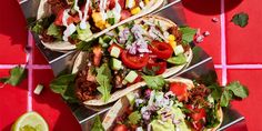 three tacos with meat, vegetables and dressing on a red tile floor next to lime wedges