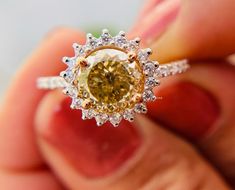 a close up of a person's hand holding an engagement ring with a yellow diamond