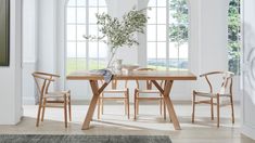 a dining room table with chairs and a vase on it in front of two windows