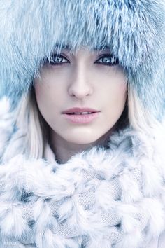 a woman with blue eyes wearing a fur hat and scarf over her head is looking at the camera