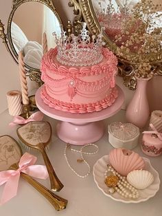 there is a pink cake with a crown on top and other items around it,