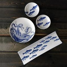 three blue and white plates with fish on them next to an octopus bowl, spoons and fork