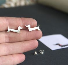 a person is holding two tiny silver dachshund studs