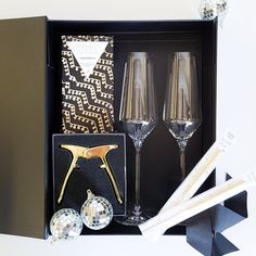 two champagne flutes in a black box with silver and gold decorations next to each other